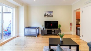 Una sala de estar con televisor, sofá, mesa de centro, un cuadro de paisaje urbano y una puerta corrediza de vidrio.