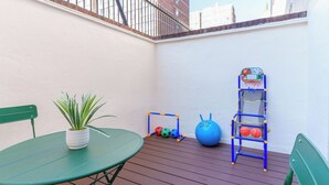 Un pequeño patio con una mesa verde, una planta en maceta, un aro de baloncesto y un soporte para balones.