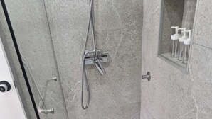 Uma área de chuveiro com porta de vidro, chuveiro manual e uma toalha no chão.