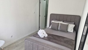 Quarto moderno com cama, um banco, uma cadeira branca e uma porta para um banheiro.