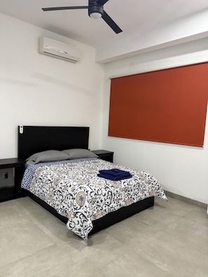 A bedroom with a bed, a nightstand, a ceiling fan, an air conditioner, and a window with a blind. - Torre Onze (Mérida)