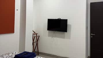 Un dormitorio con cama, ventilador de techo, televisor montado en la pared y una puerta.