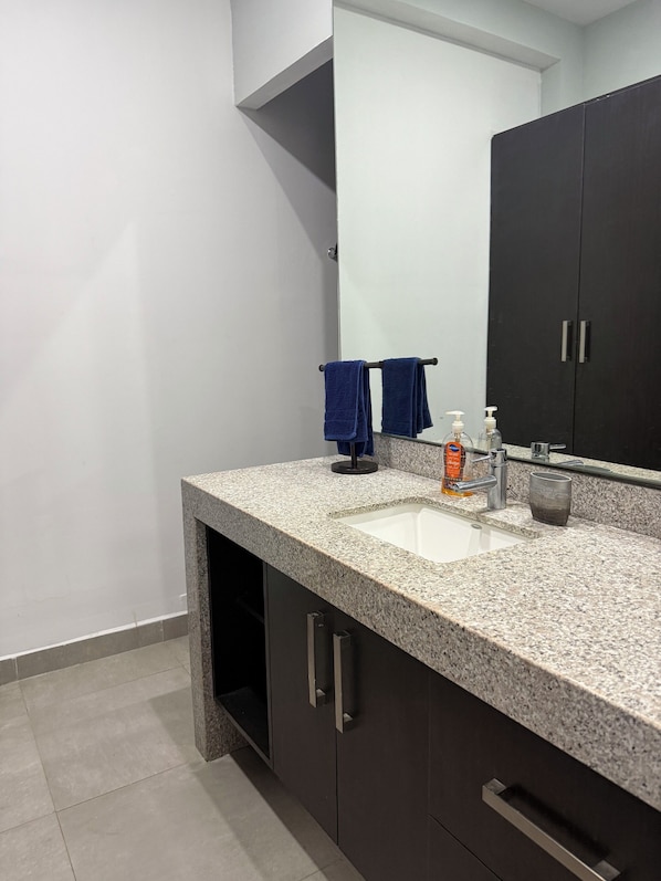 A bathroom with a granite countertop, a sink, a mirror, a dark cabinet, and a towel rack. - Torre Onze (Mérida)