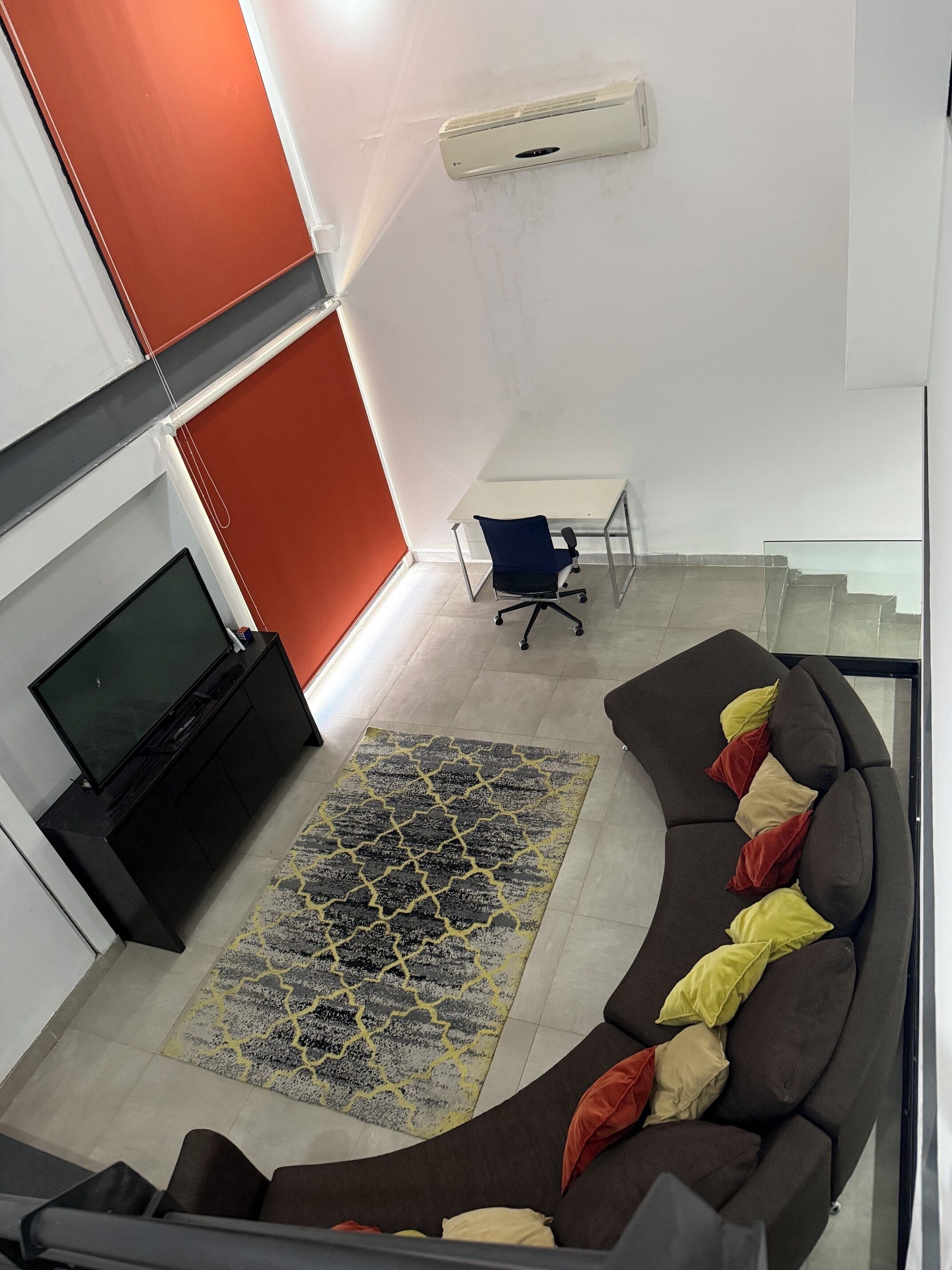 Een moderne woonkamer met een gebogen bank, een flatscreen televisie, een vloerkleed met dessin en een airconditioning.