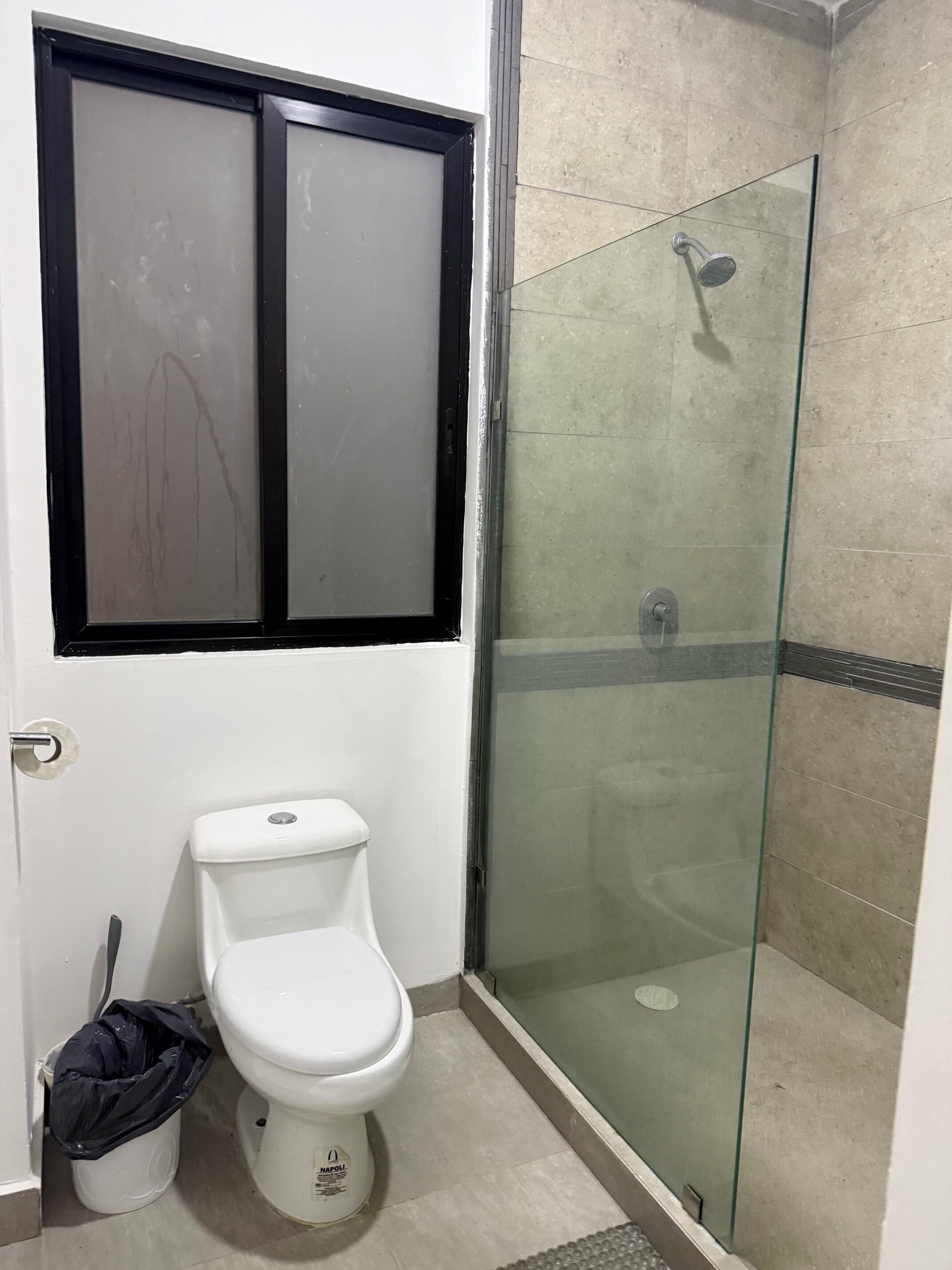 Un baño con inodoro, cabina de ducha de vidrio y ventana con marco negro.