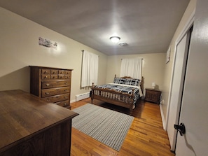 A bedroom with a wooden dresser, a bed with a patterned bedspread, a radiator, and a door. - 3 Bedroom House - Family Friendly - Sleeps 6 (Ephrata)