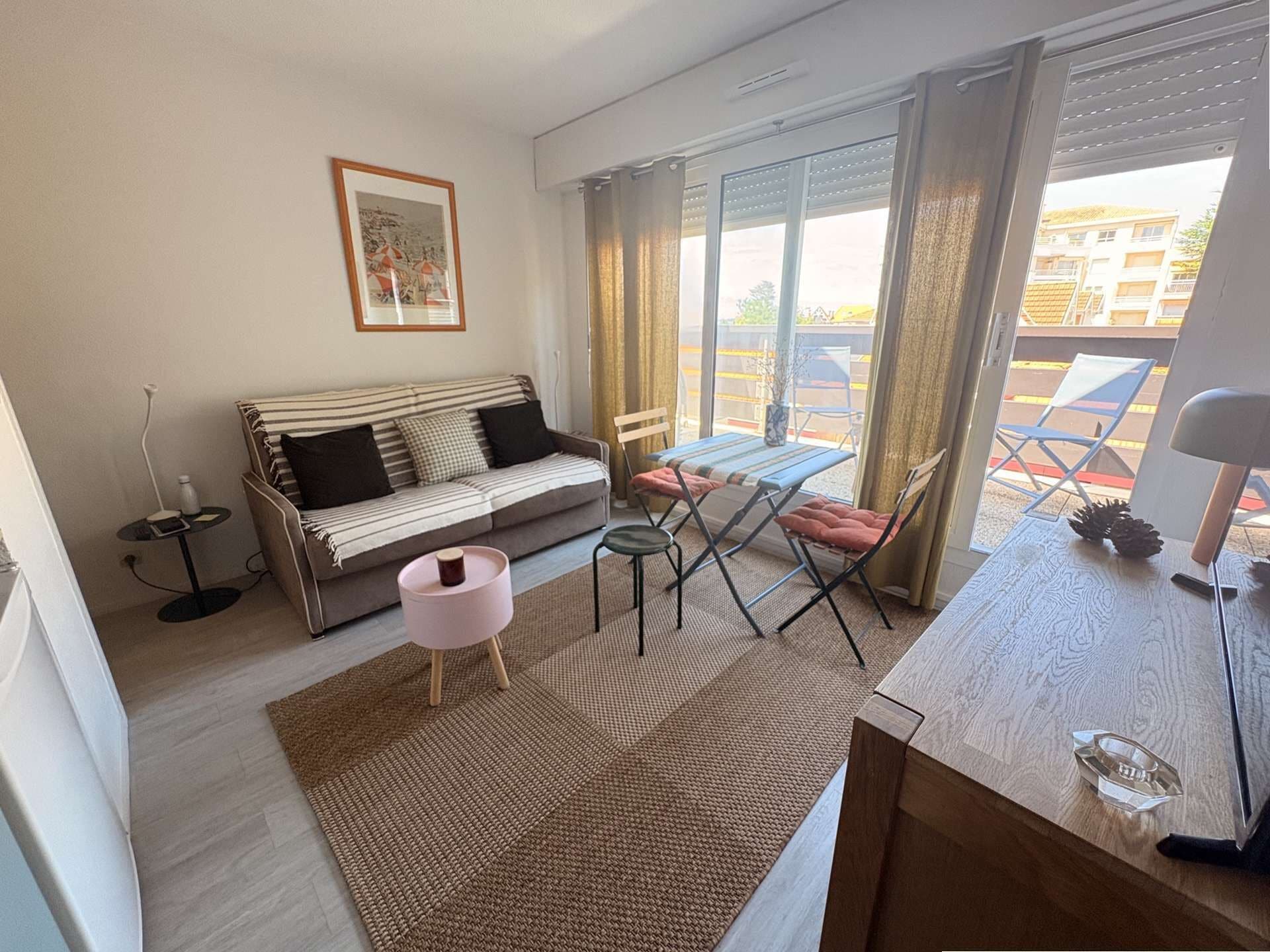 Una sala moderna con un sofá, una mesa de comedor con sillas, una pequeña mesita auxiliar y un amplio ventanal con cortinas.