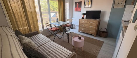Una sala de estar acogedora con un sofá, una mesa de comedor con sillas, un televisor y una zona de cocina con armarios.