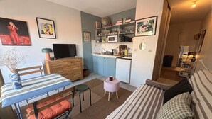 Un espace de vie compact comprenant un coin cuisine, un coin repas et un coin salon avec un canapé et un fauteuil.