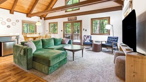 Una sala acogedora con un sofá seccional verde, una mesa de comedor de madera y un televisor.