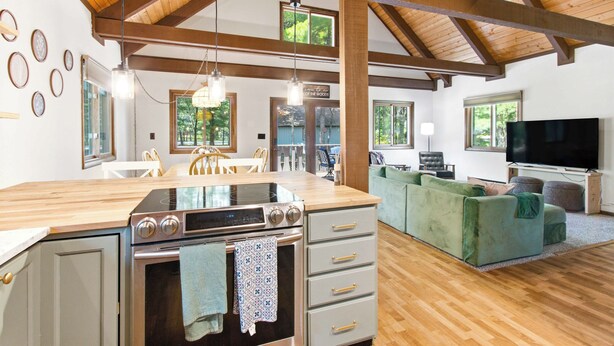Una cocina moderna con una isla grande, vigas de madera en el techo y un comedor con sillas.