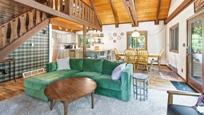 Amplia sala de estar con un sofá verde, una mesa de centro de madera y una escalera que conduce a un nivel superior.