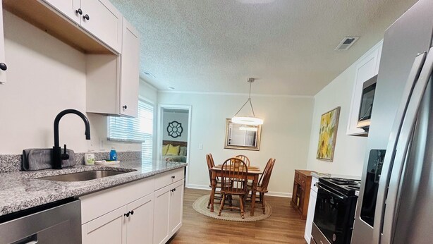 A modern kitchen with white cabinets, a stainless steel refrigerator, and a dining area with a wooden table and chairs.