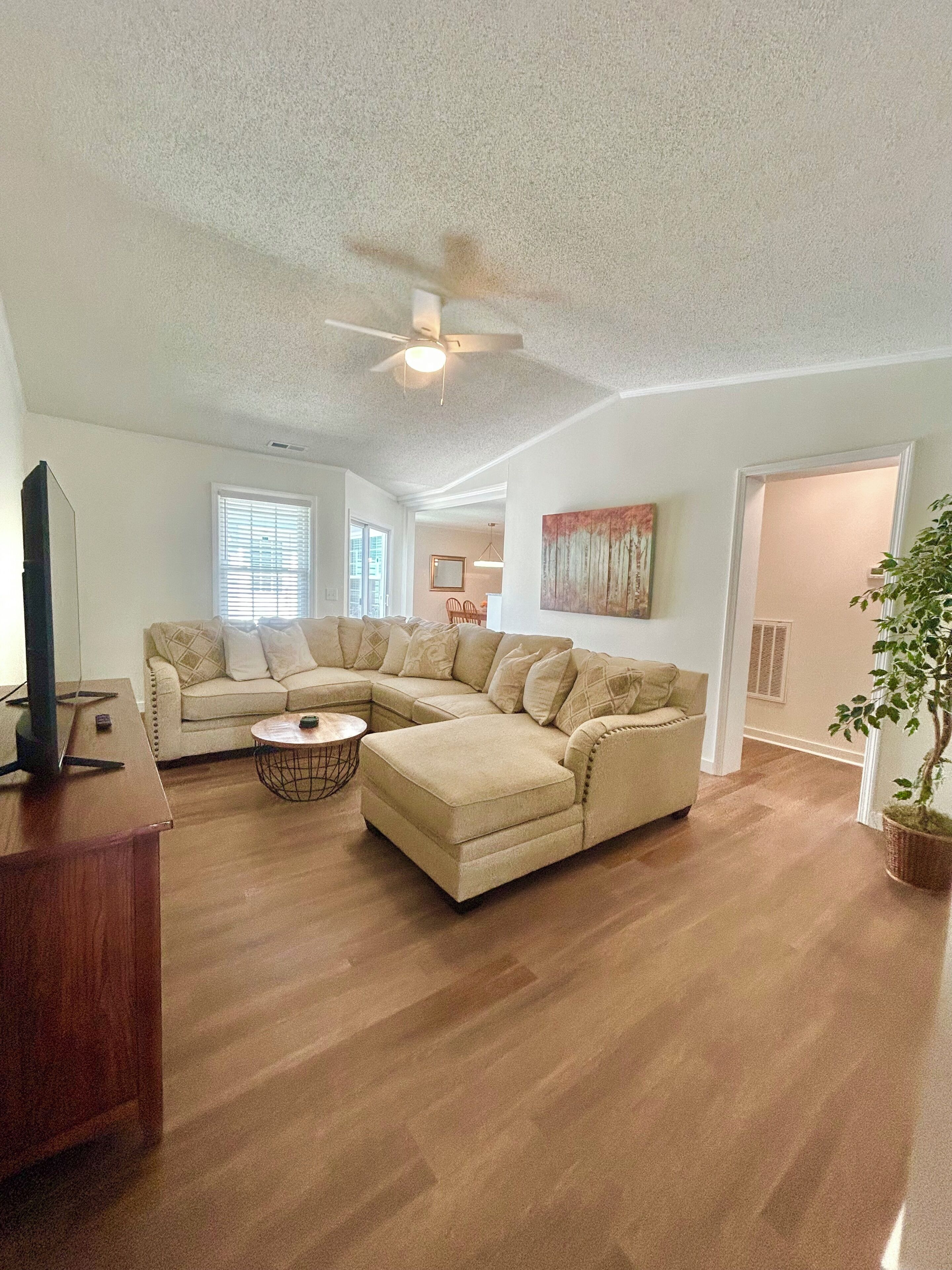 A living room with a sectional sofa, a coffee table, a television on a stand, and a ceiling fan.