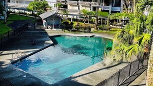 En swimmingpool omgiven av en terrass, en byggnad med flera balkonger och frodig, tropisk växtlighet.
