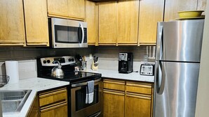 A kitchen with wooden cabinets, a stainless steel refrigerator, a microwave, a stove, and a coffee maker. - Gateway to Adventure! (Durango)