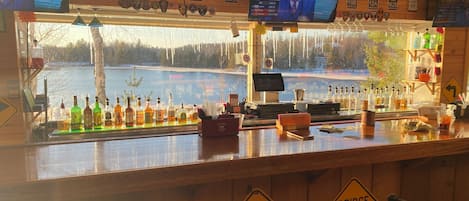 Un bar con vistas a un lago, múltiples televisores y letreros que indican un puente más adelante.