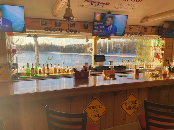 A bar with a view of a lake, multiple televisions, and signs indicating a bridge ahead. - Clevelands clubhouse at Beaver Lodge (Mercer)