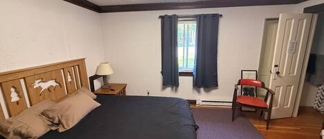 A bedroom with a bed, a nightstand, a chair, a window with curtains, and a door.