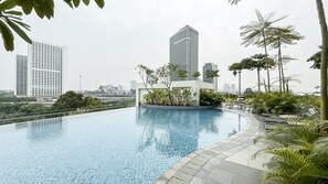 A swimming pool with a tiled edge, surrounded by greenery and a view of tall buildings. - Studio Minimalist Areum Residence At Antasari Place (Jakarta)