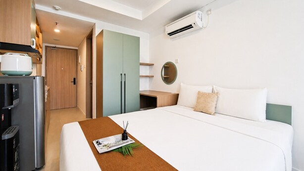 A hotel room with a bed, a coffee machine, a refrigerator, a desk, and an air conditioning unit. - Studio Minimalist Areum Residence At Antasari Place (Jakarta)