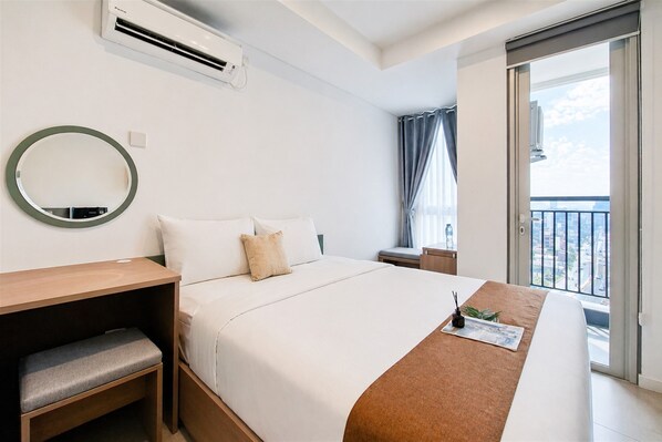 A hotel room with a bed, bedside tables, a mirror, and a view of the city through a balcony. - Studio Minimalist Areum Residence At Antasari Place (Jakarta)