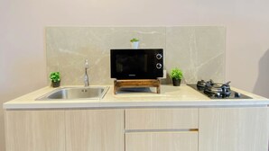 A kitchen with a built-in microwave, sink, and stove. There are two potted plants on the counter. - Homey Gray Studio Room At Apartment Antasari Place (Jakarta)