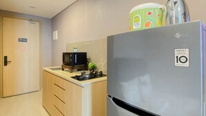 A compact kitchen with a stainless steel refrigerator, a microwave on a wooden stand, and a small gas stove. - Homey Gray Studio Room At Apartment Antasari Place (Jakarta)