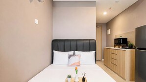 A modern bedroom with a bed, bedside table, and a small kitchenette area. - Homey Gray Studio Room At Apartment Antasari Place (Jakarta)