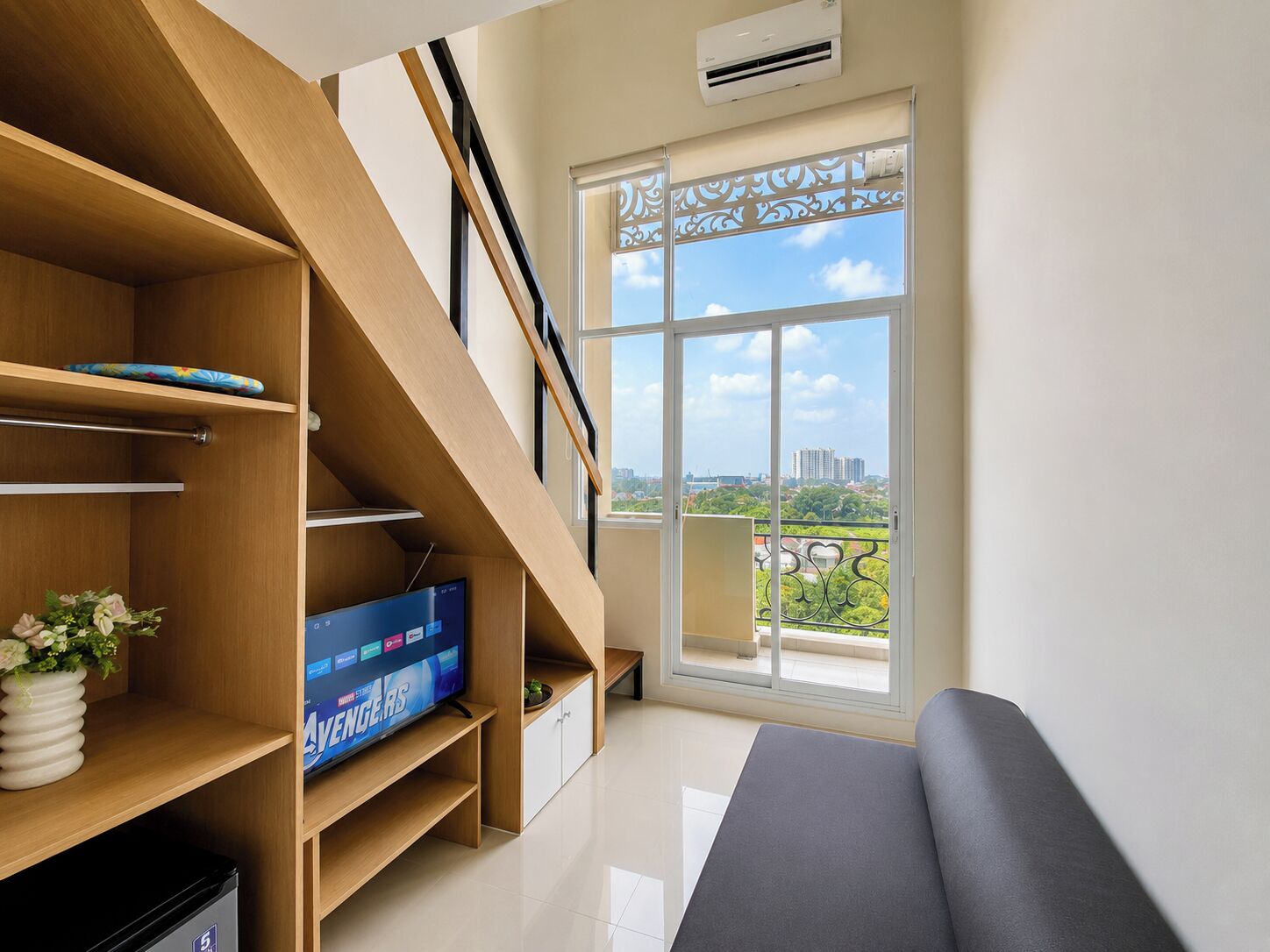 A modern room with a staircase, a flat-screen TV, a sofa, and a large window with a view of the city.