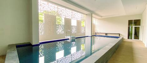Una piscina con borde azul, rodeada por un muro blanco con paneles decorativos y un suelo de madera.