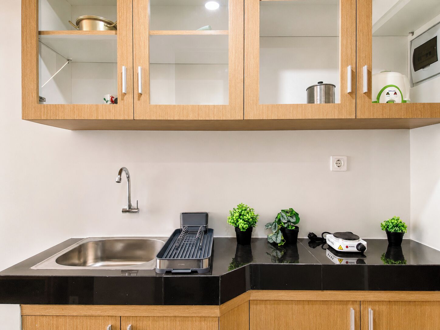 A kitchen with a stainless steel sink, a black countertop, wooden cabinets, and a microwave.