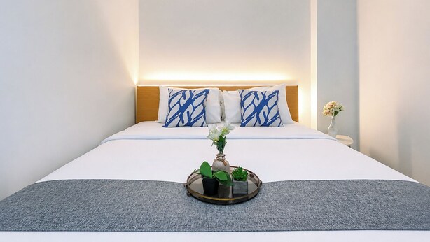 Ein Hotelzimmer mit einem Bett, einem Nachttisch mit Blumenvase und einem Tablett mit Pflanze.