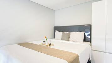 A hotel room with a bed, a bedside table with a tray, a wardrobe, and a plain white wall.