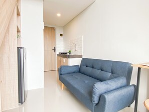 Un espacio de estar moderno con sofá, refrigerador y zona de cocina con salpicadero de azulejos.
