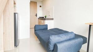 Et moderne værelse med seng, lille bord, køleskab og et tekøkken med vask og bordplade.