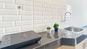 Et køkken med hvide metrofliser, en rustfri stålvask og en sort induktionskogeplade.