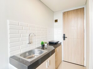 A kitchen with a stainless steel sink, a black countertop, and wooden cabinets. - Practical Studio Loft At Apartment Apple 3 Condovilla (Jakarta)