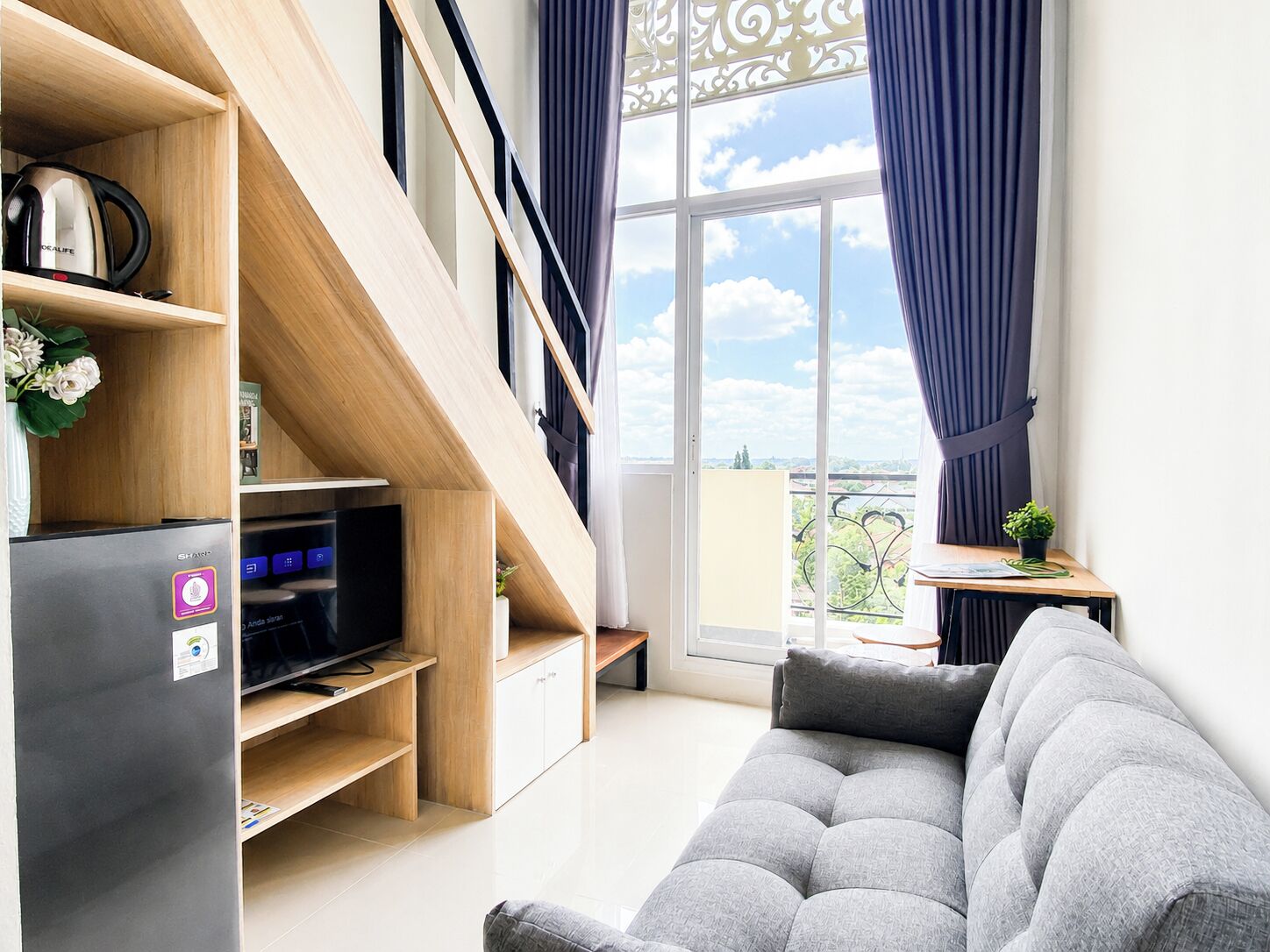 Una sala moderna con sofá, televisor de pantalla plana, refrigerador y una escalera.