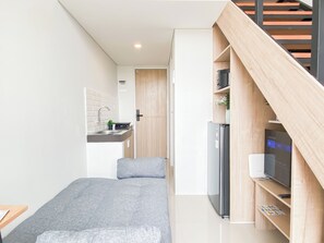 A compact living space with a kitchenette, a bed, and a built-in TV. - Practical Studio Loft At Apartment Apple 3 Condovilla (Jakarta)