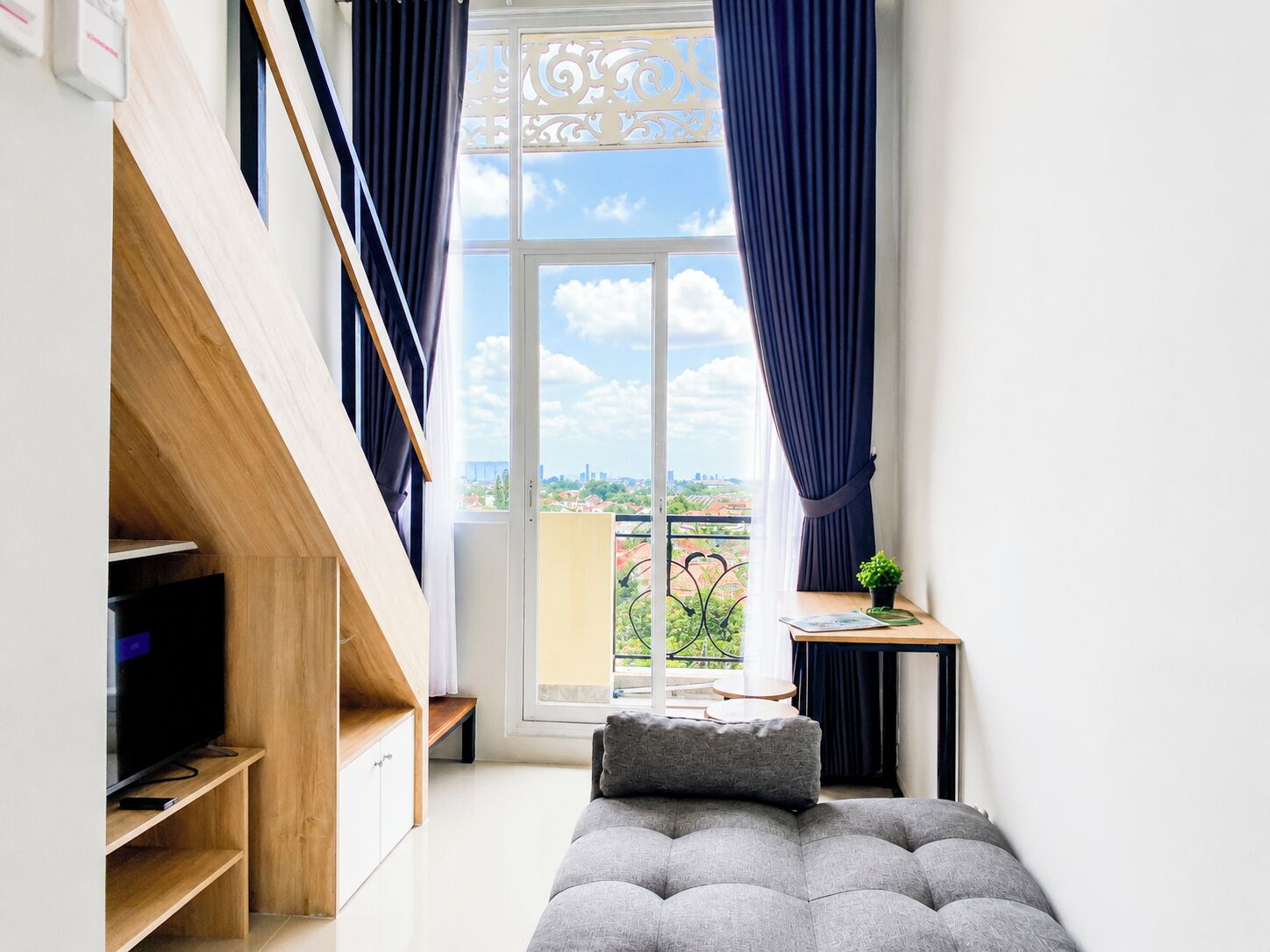 Un dormitorio moderno con un ventanal amplio, un televisor de pantalla plana, un sofá y una pequeña mesa con una planta.