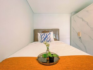 A hotel room with a bed, a bedside table with a tray of plants, a marble wall, and a door with a key lock. - Smart Urban Loft Studio At Apartment Apple 3 Condovilla (Jakarta)