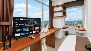 A modern office space with a large flat-screen TV displaying a streaming service interface, a wooden desk with a smartphone, and a city view through large windows.
