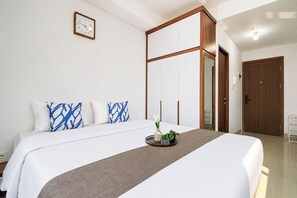 Une chambre d’hôtel avec un grand lit, une table de chevet agrémentée d’un vase et de plantes, une horloge au mur et une armoire en bois.