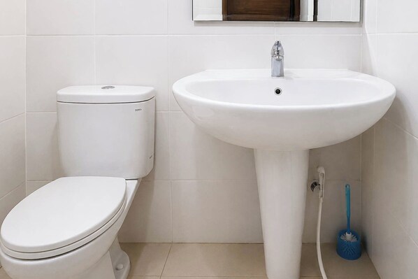 A bathroom with a white toilet, a white sink, and a blue cleaning brush.