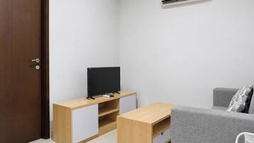 A small, modern room with a wooden TV stand, a grey sofa, and a white air conditioning unit.