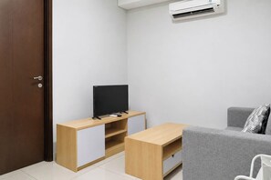 A small, modern room with a wooden TV stand, a grey sofa, and a white air conditioning unit.