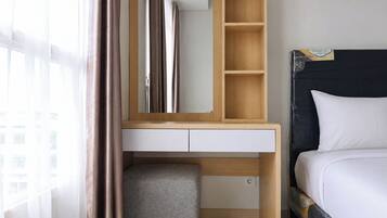 A hotel room with a bed, a bedside table with a mirror, a small stool, and a window with curtains.