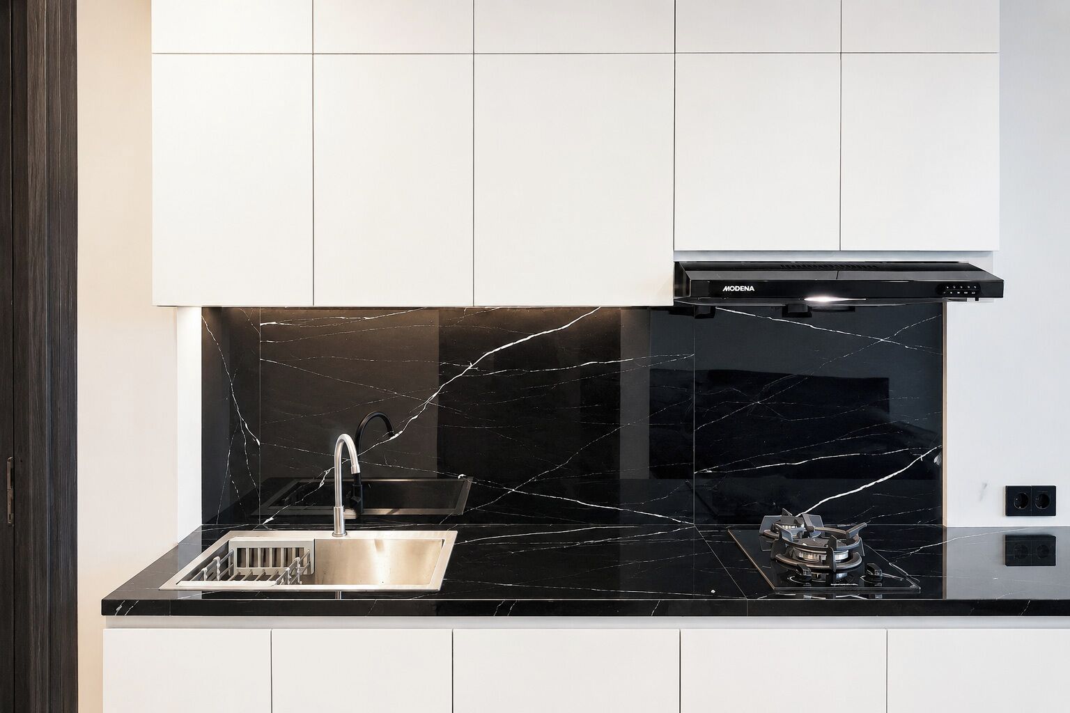Uma cozinha moderna com painel de parede em mármore preto, pia de aço inoxidável e exaustor preto.