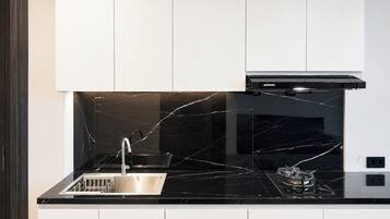 Uma cozinha moderna com painel de parede em mármore preto, pia de aço inoxidável e exaustor preto.